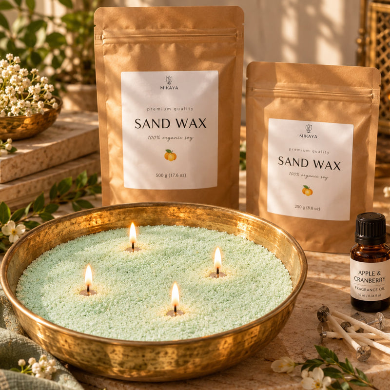 Green sand wax candle in a brass urli with four lit wicks, beside 250 g and 500 g Mikaya sand wax pouches, fragrance oil and wicks