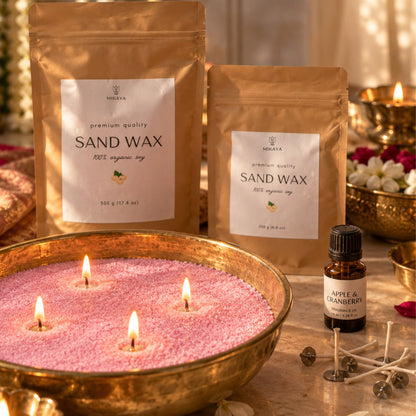 Pink sand wax candle in a brass urli with four lit wicks, beside 250 g and 500 g Mikaya sand wax pouches, fragrance oil and wicks